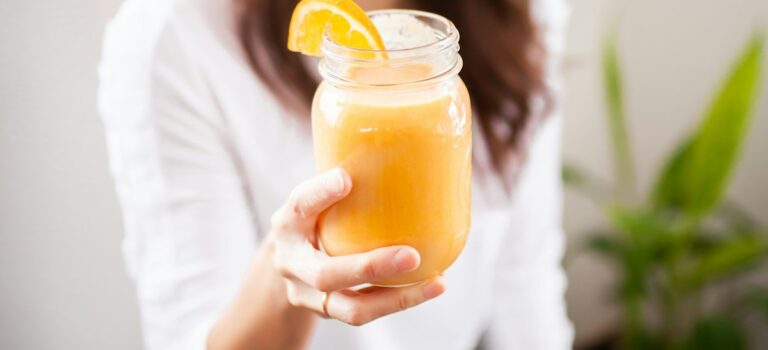 smiling woman holding clear glass jar with yellow liquid